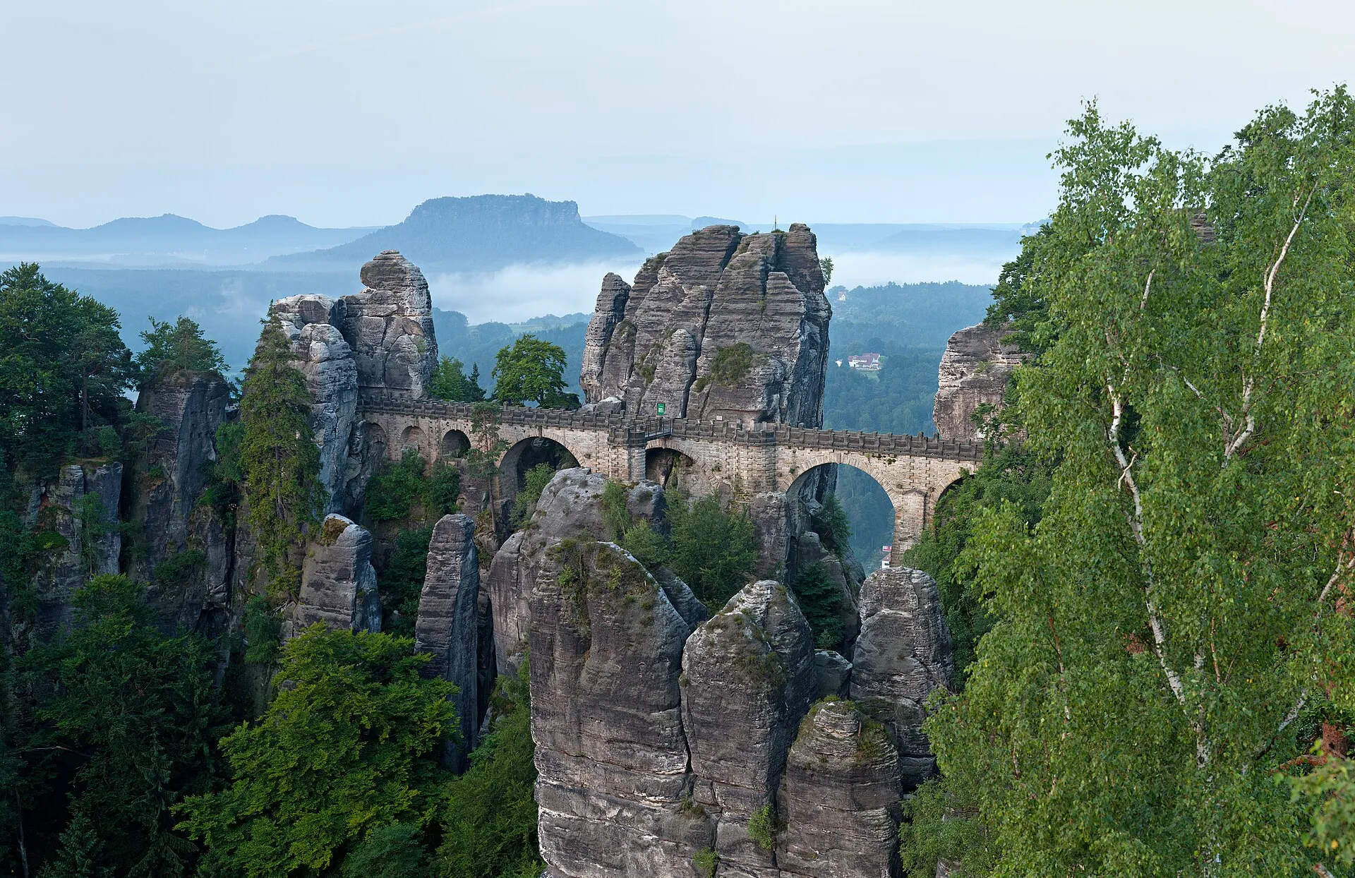 Basteibrücke zwischen Sandsteinfelsen im Morgendunst, im Hintergrund der Tafelberg Lilienstein