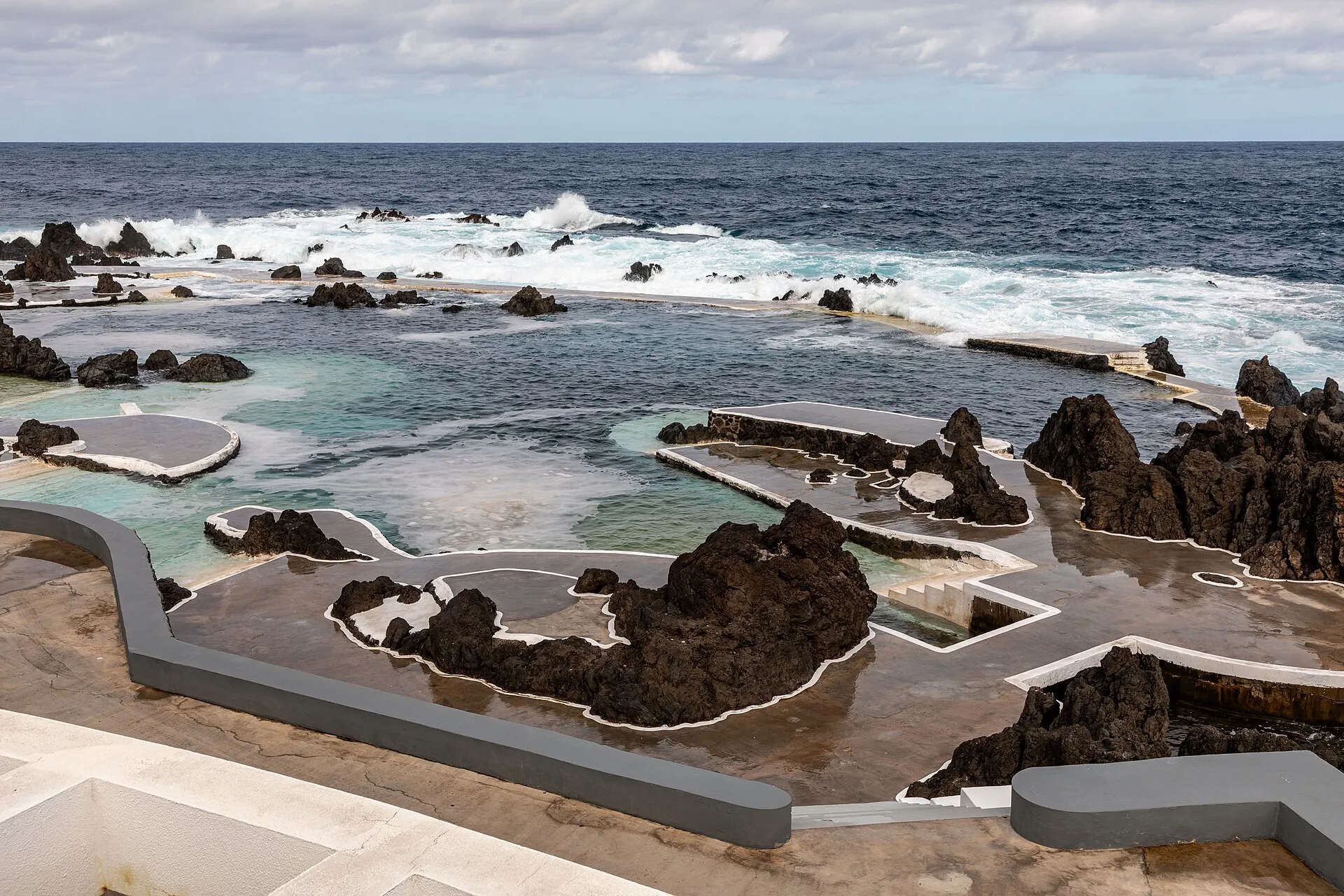 Naturschwimmbecken von Porto Moniz zwischen schwarzen Lavafelsen, dahinter Brandung am offenen Atlantik